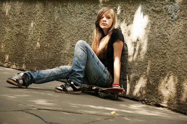 The girl with skateboard sitting against awall